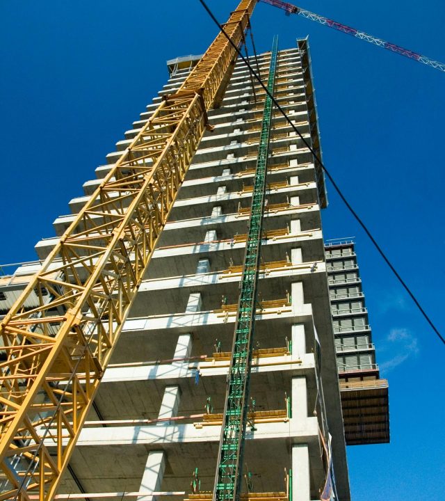 Low-angle view of skyscraper under construction with crane, clear blue sky.
